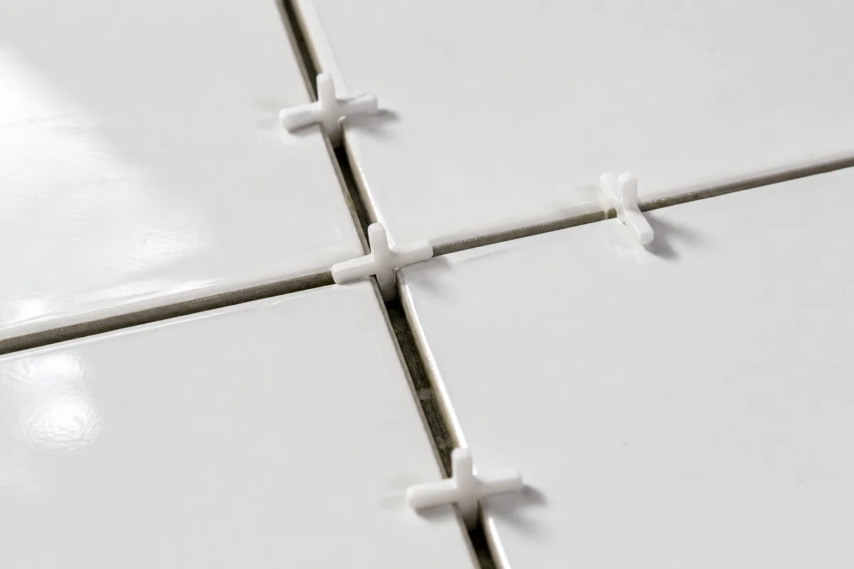 Croisillons en plastique insérés entre des carreaux muraux blancs fraîchement posés